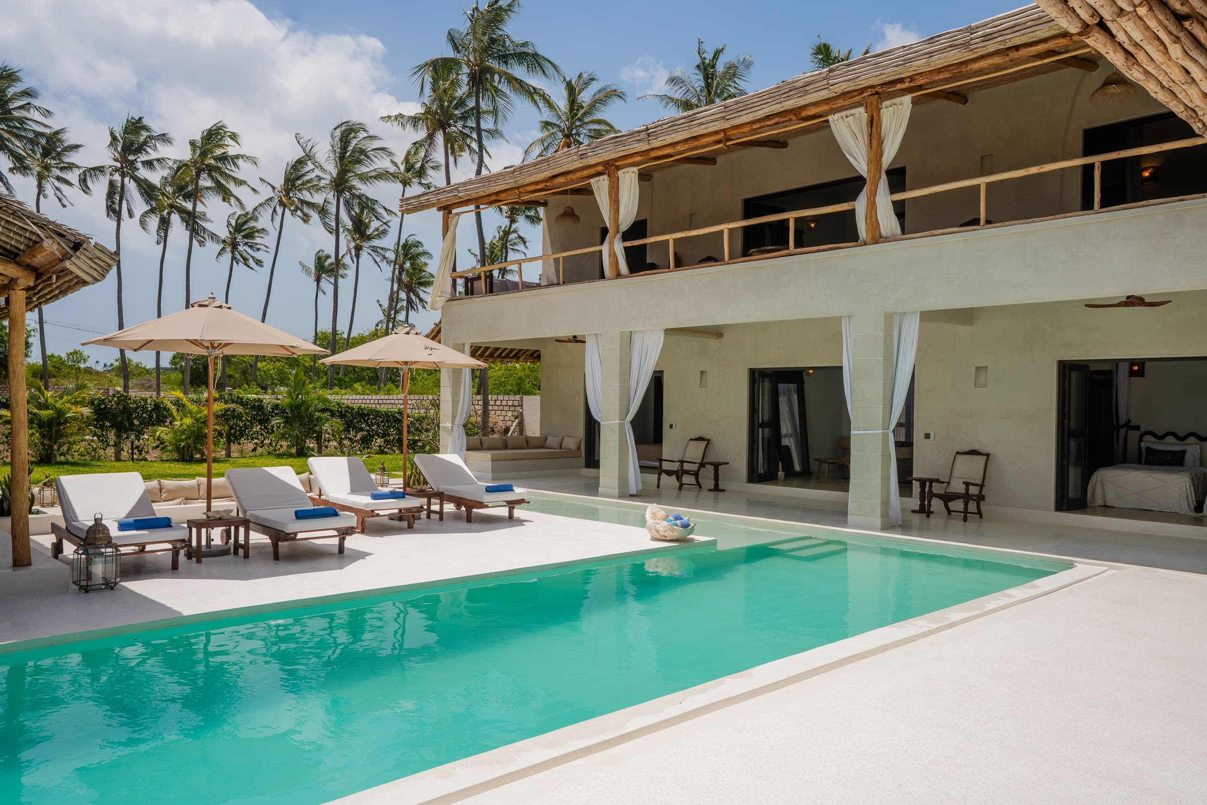 Beachfront villa exterior with infinity pool, lounge chairs, and palm trees