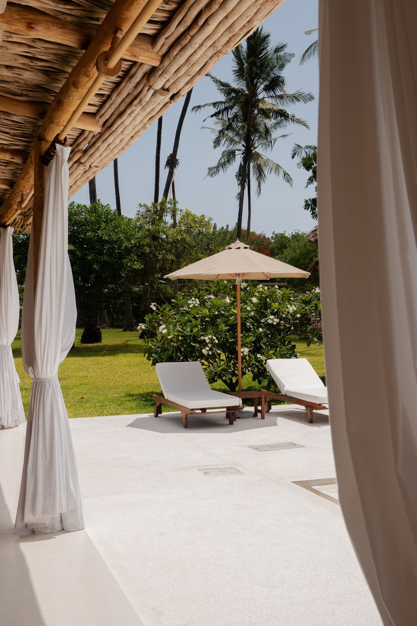 Poolside lounge area with sunbeds under umbrellas and tropical plants