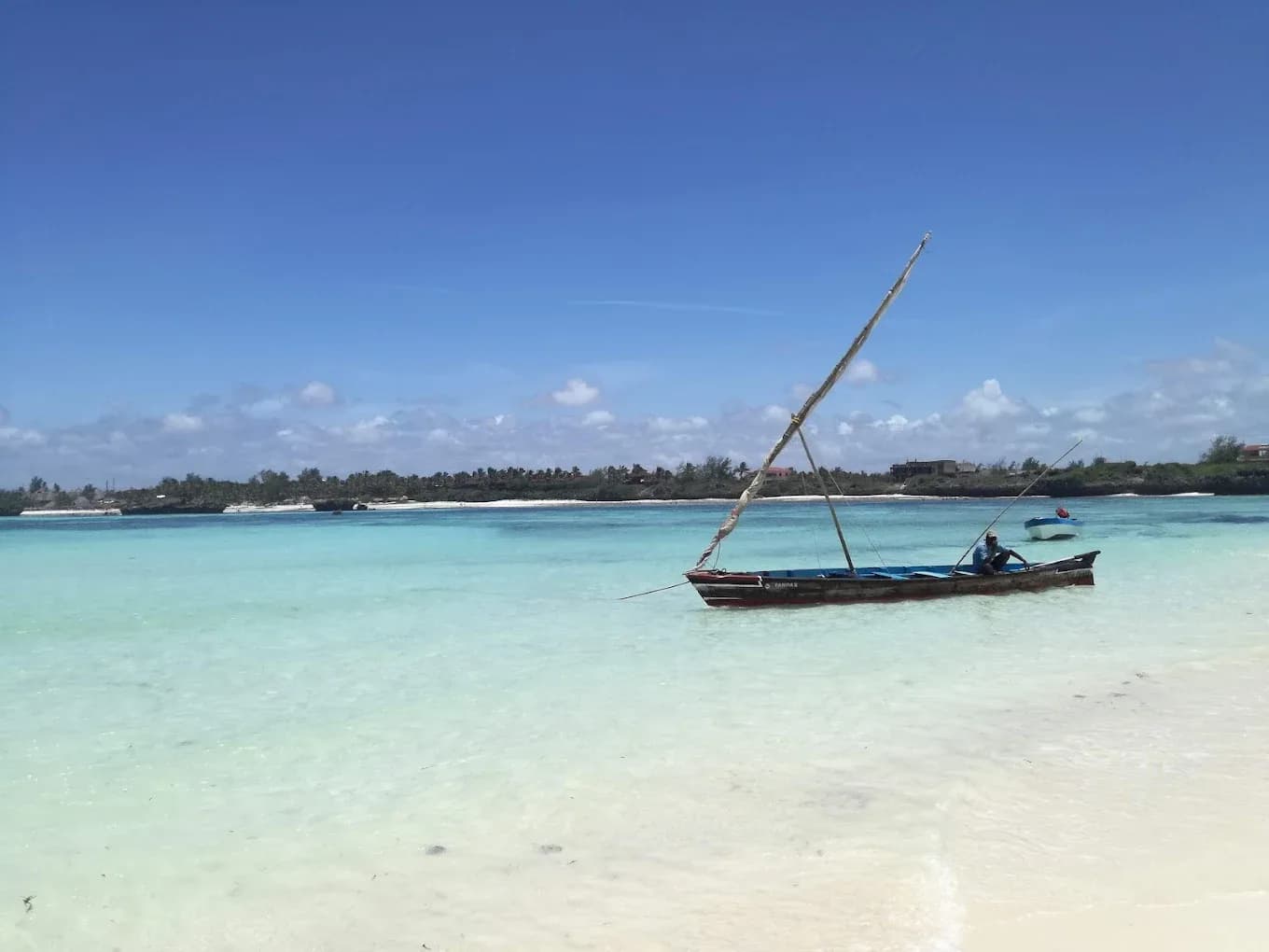 Traditional dhow sailboat in turquoise shallow waters near white sandy beach